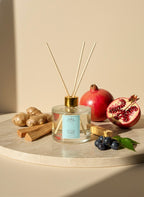 Reed diffuser with pomegranates, cinnamon sticks, and blueberries on a beige surface